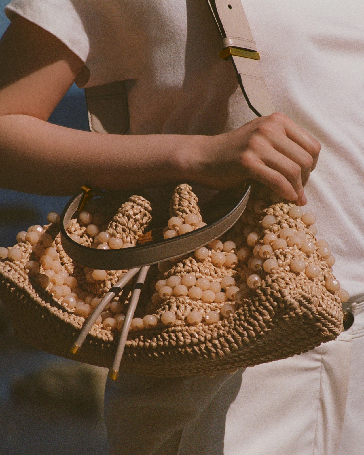 Model holding red gingham wedges with bow while leaning on a seaside railing.	