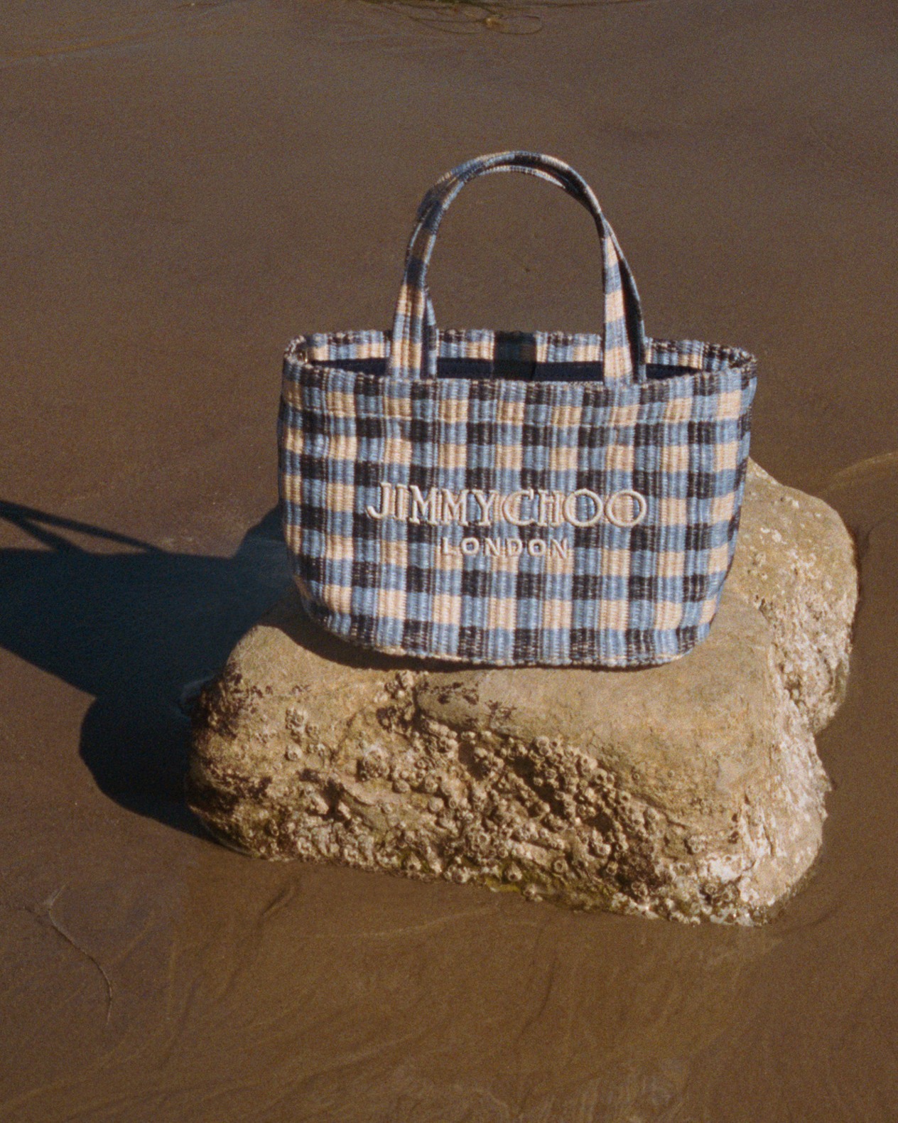 Model holding red gingham wedges with bow while leaning on a seaside railing.	