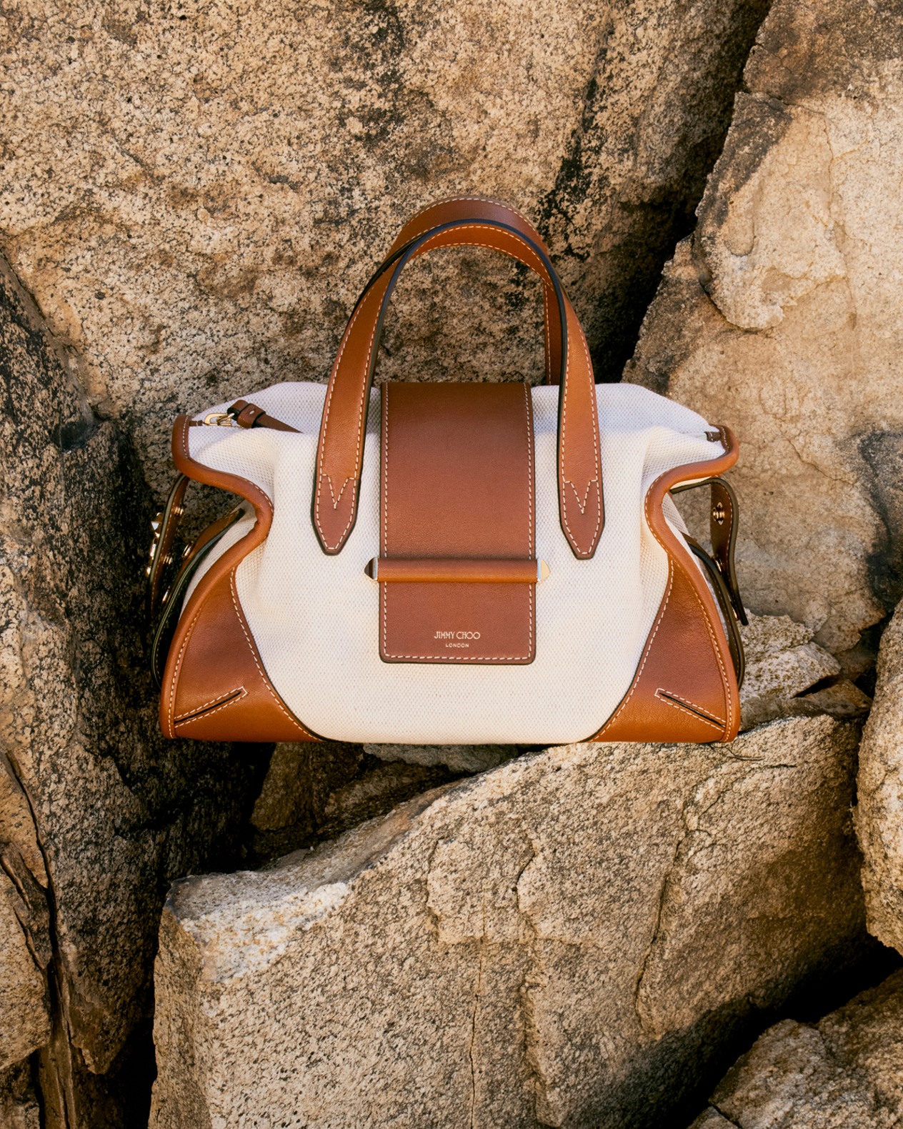Beige flat sandals with textured fringe straps placed on rocky ground.