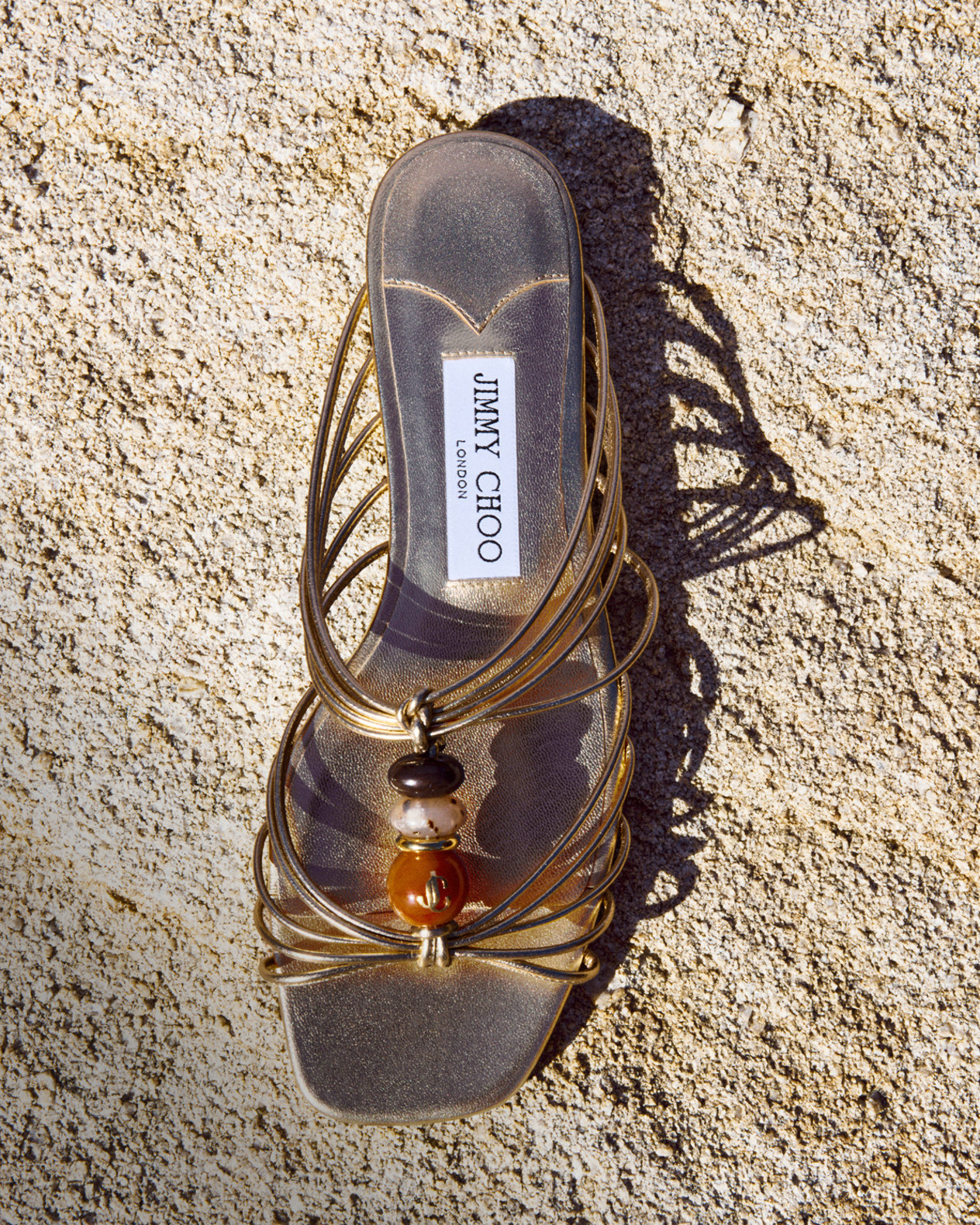 Metallic sandal with bead embellishment placed on textured rock.