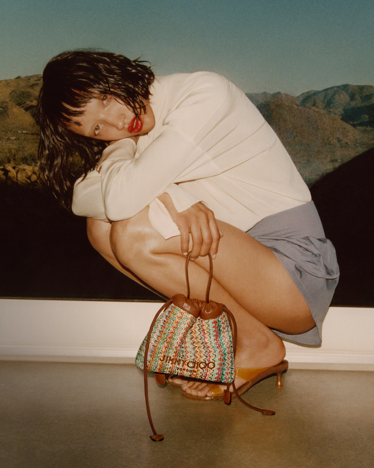Beige flat sandals with textured fringe straps placed on rocky ground.