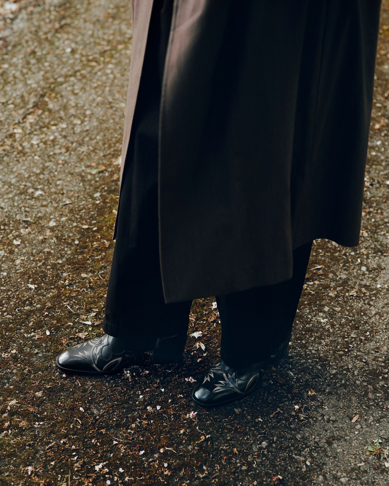 Close-up of black loafers with rose print detailing worn with wide-leg black trousers outdoors.