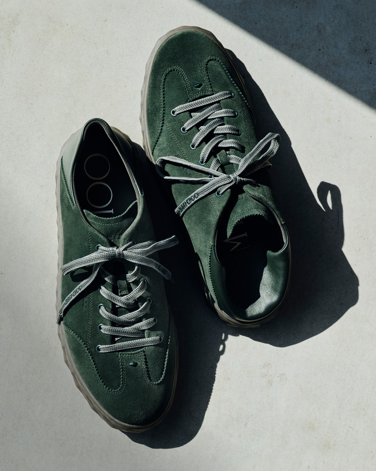 Close-up of a woman&rsquo;s legs wearing pale green pointed slingback heels with floral detailing, standing on a brick floor.	