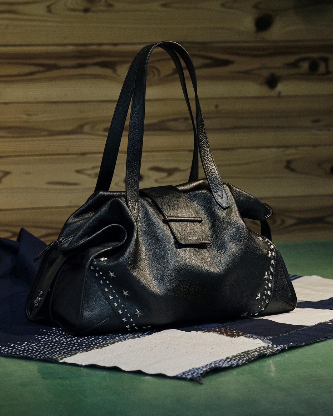 Mint green top-handle handbag with structured silhouette placed on a brick floor against a textured stone wall.	