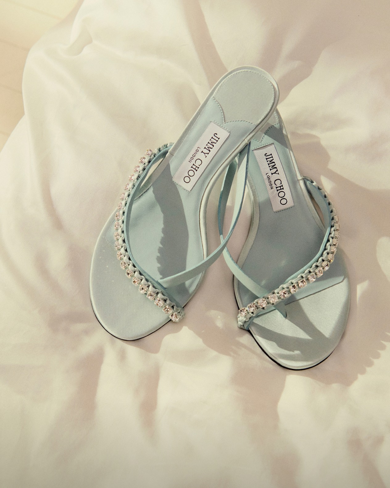 Pair of heeled sandals with crystal-embellished straps, placed on a cream fabric surface.