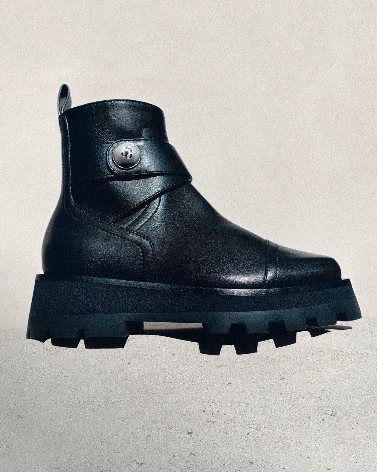 Black leather biker boots with buckle detailing, photographed against a green textured backdrop.