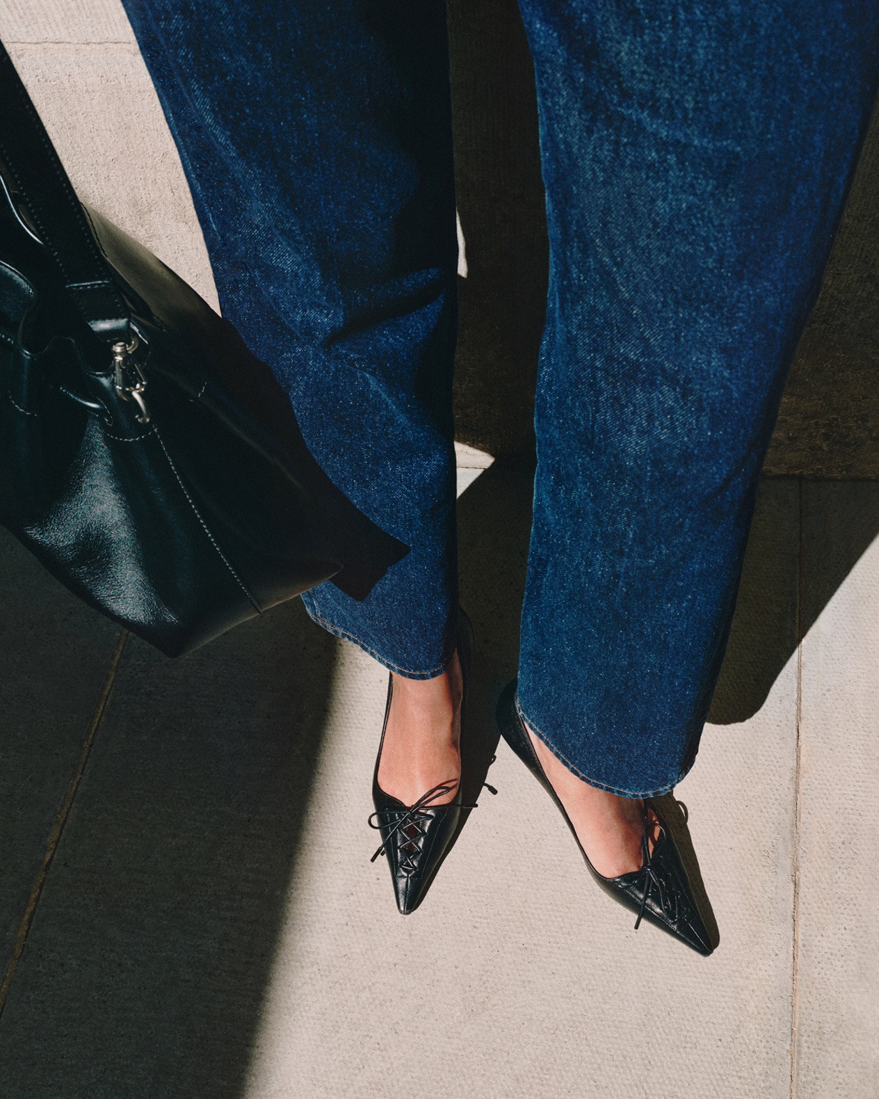 Woman holding an oversized brown suede bag under her arm, styled with a minimal black slip dress.