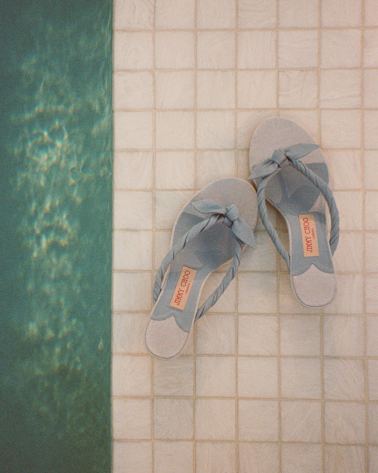 Blue bow-detail heeled sandals placed on a tiled poolside surface.