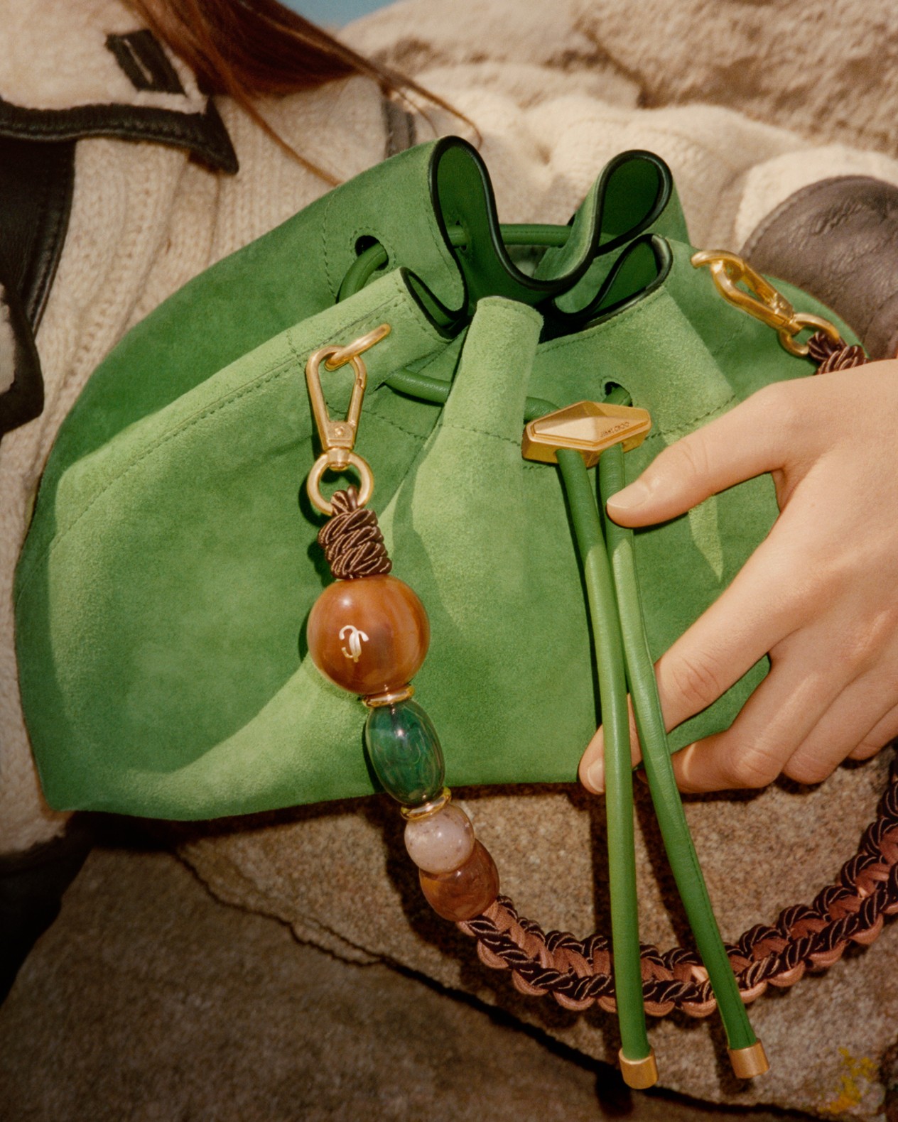 Green suede drawstring bag with a beaded and woven chain strap resting beside a model.