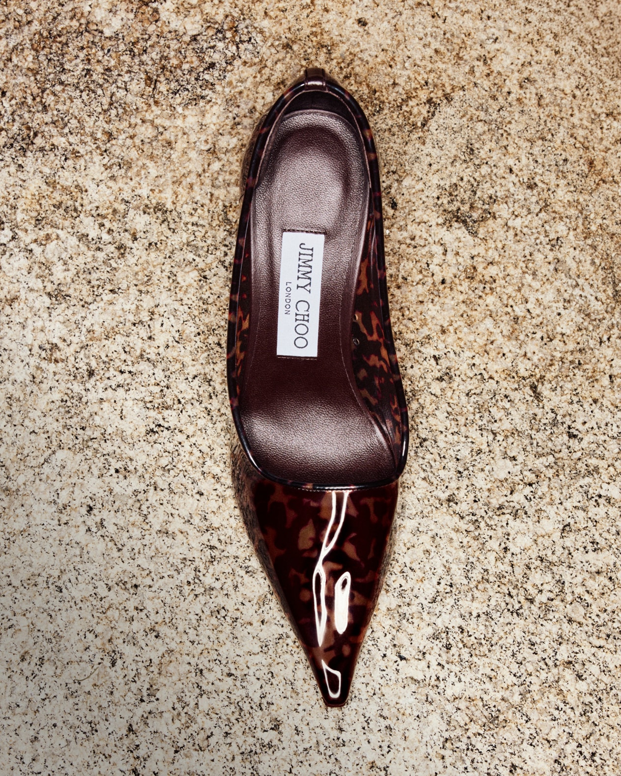 Tortoiseshell-print pointed-toe pump displayed on a textured stone surface.