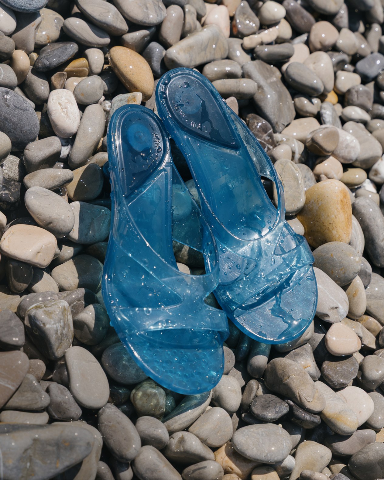 Pair of translucent blue jelly sandals on smooth pebbles.	