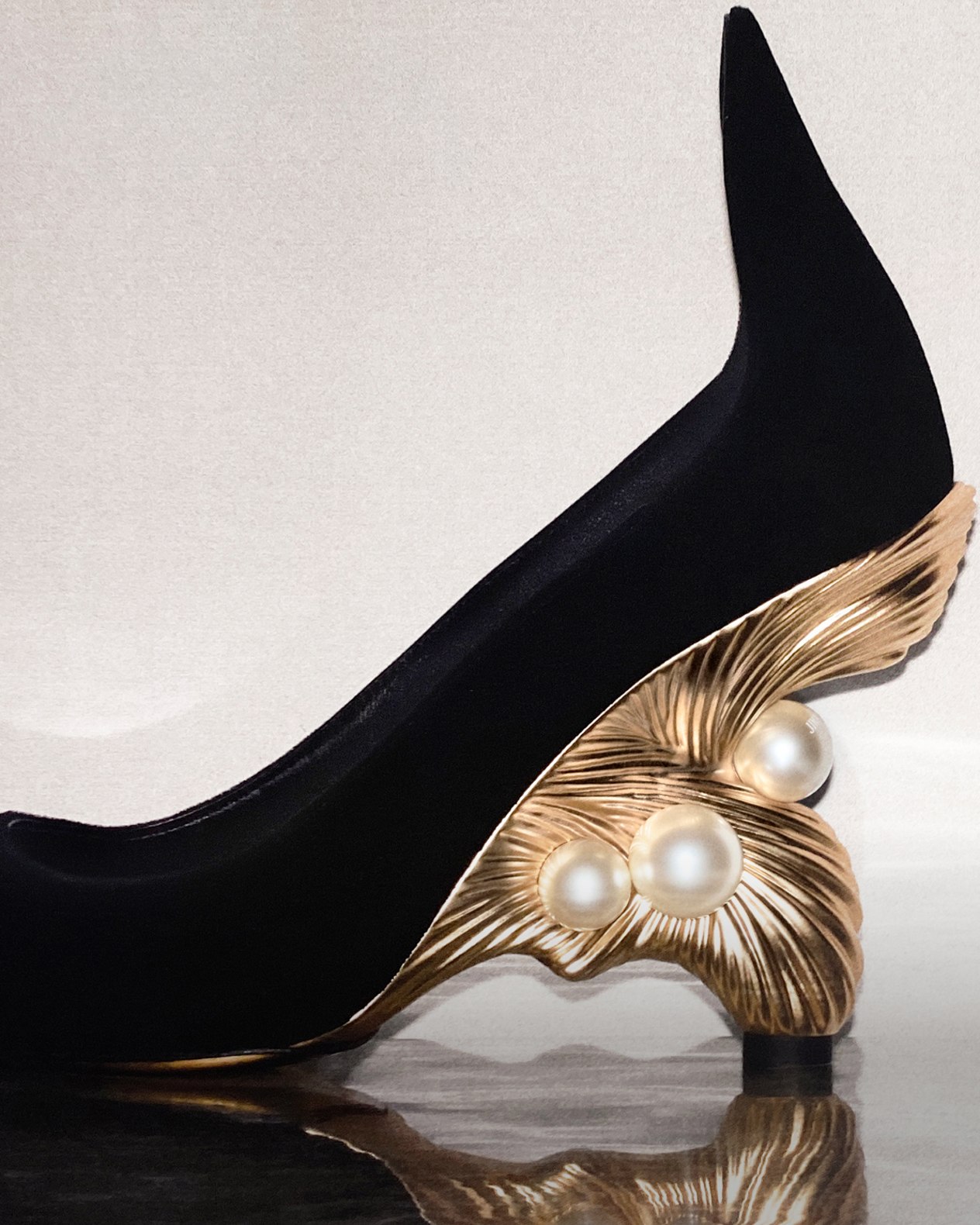 Close-up of a black pointed-toe pump with a sculptural gold heel and pearl detailing.