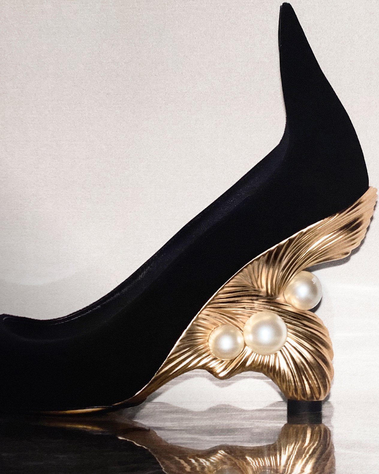 Close-up of a black pointed-toe pump with a sculptural gold heel and pearl detailing.
