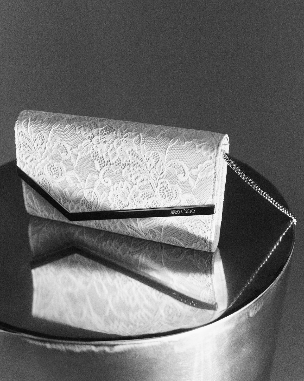 Tan leather top-handle bag with stud and pearl detailing, styled against green foliage.