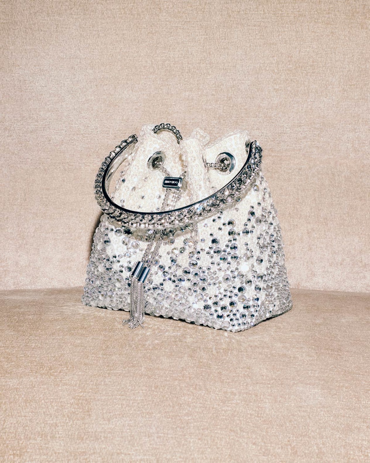 Crystal embellished Bon Bon bag with a jeweled handle and tassel detail, displayed against a neutral fabric background.