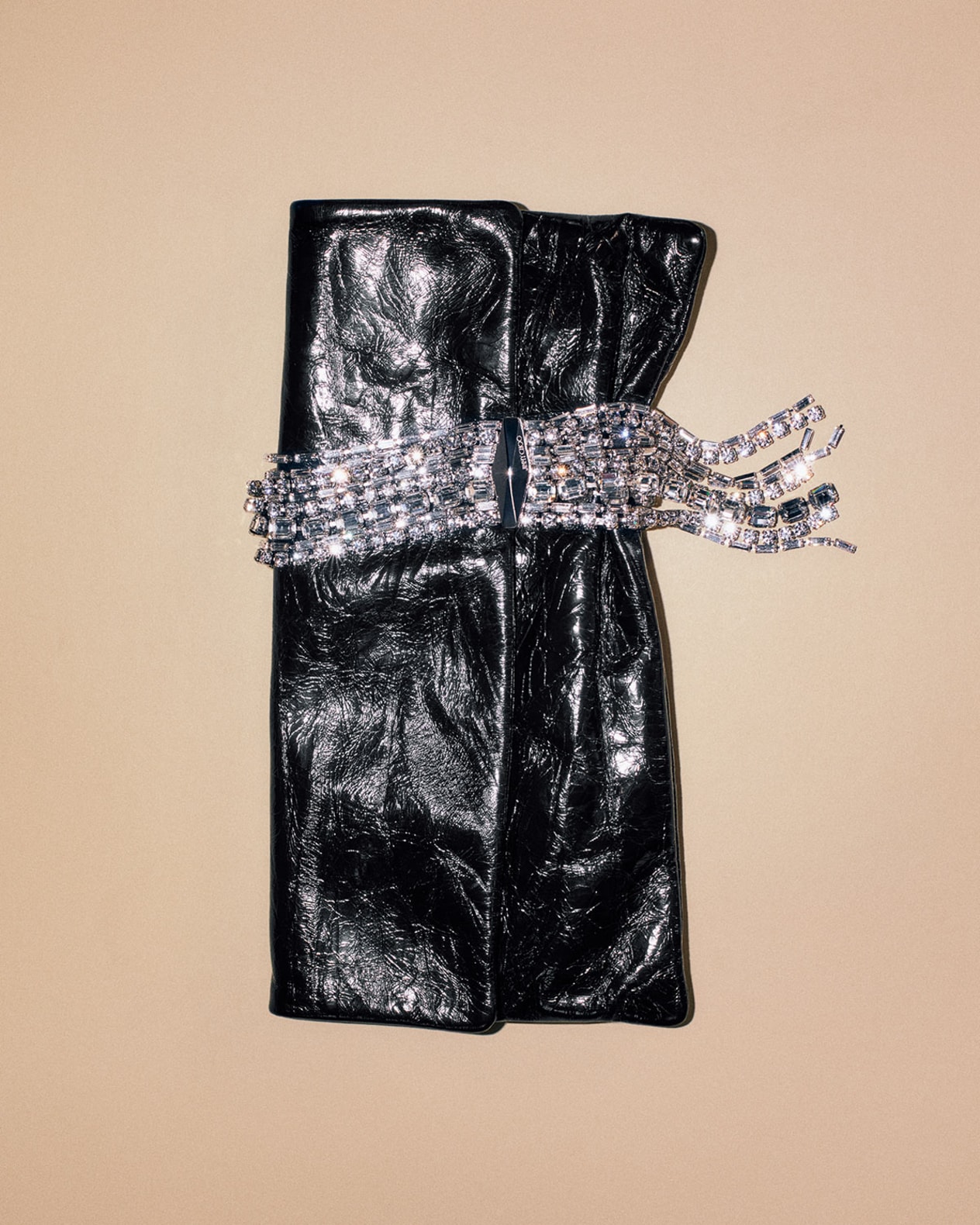 Black leather clutch detailed with a sparkling crystal fringe, displayed against a neutral fabric background.