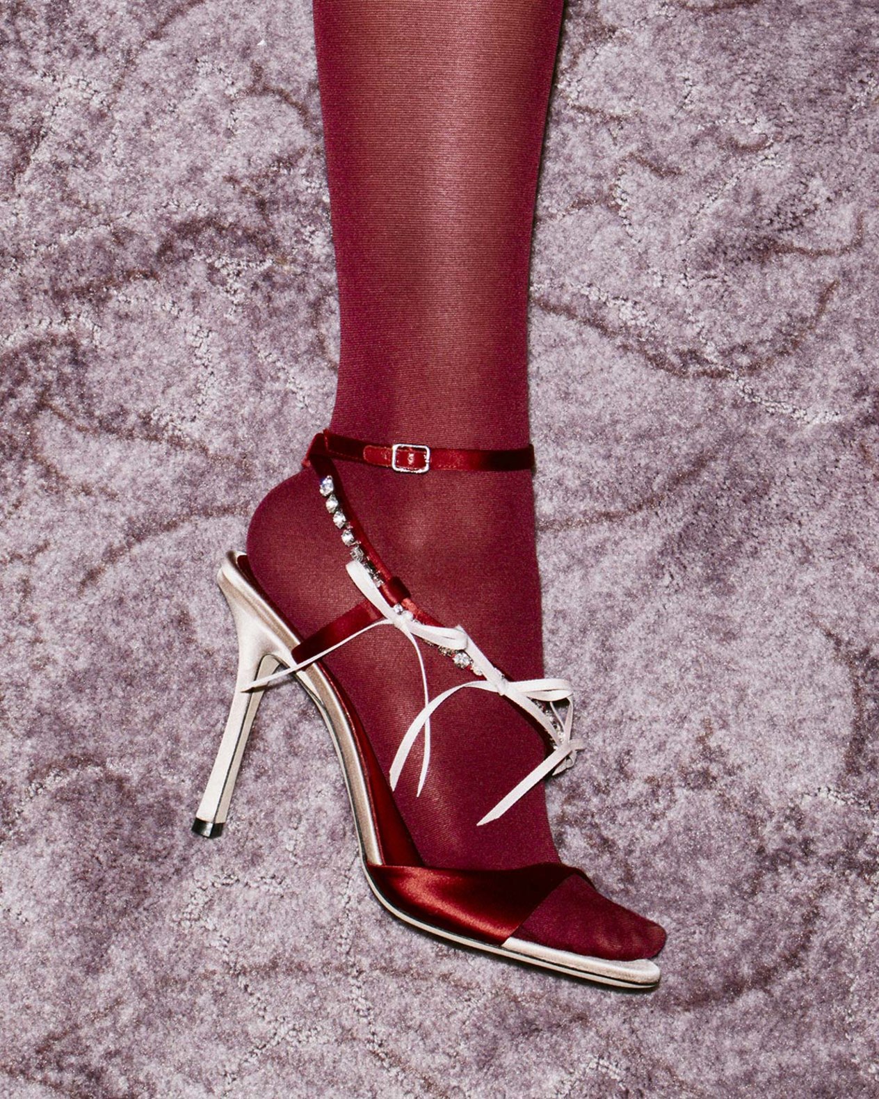 Red high-heeled sandal displayed against a patterned gold backdrop.