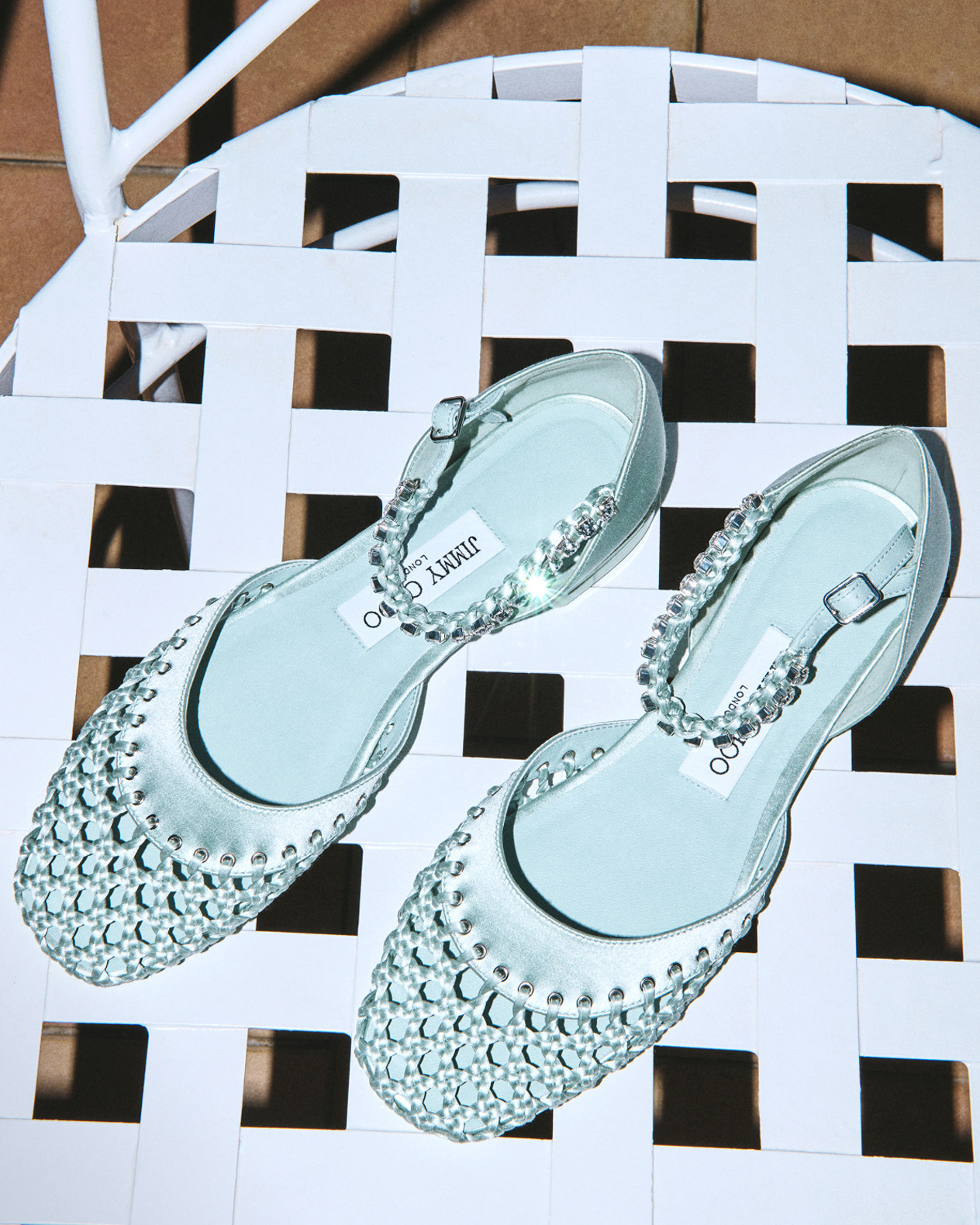 Mint green mesh flats with crystal embellishment on a white woven chair.