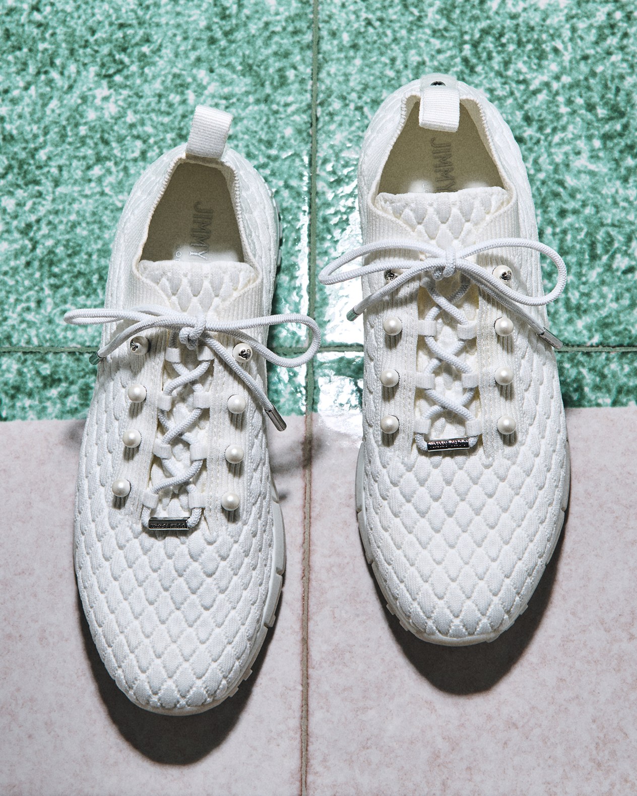 White textured lace-up sneakers placed on two-tone green and stone tiles.