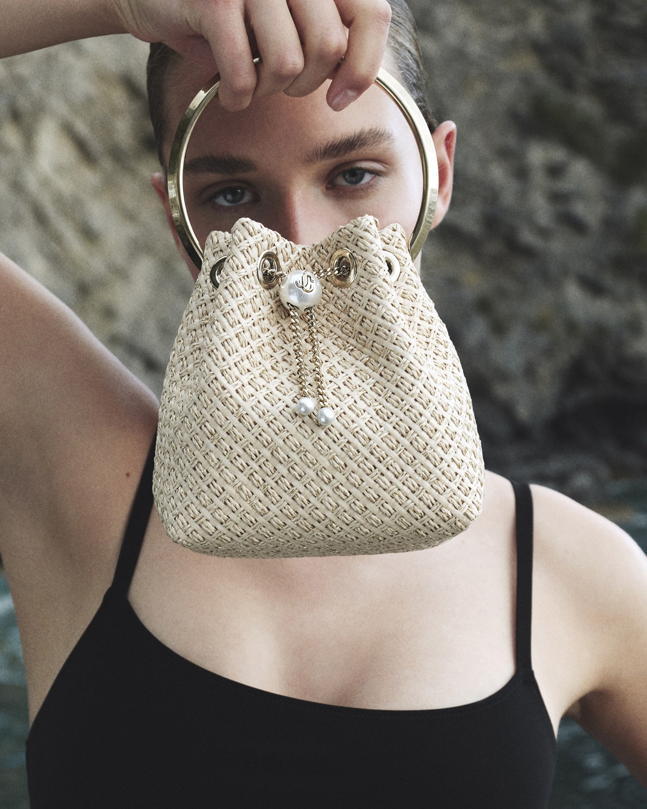 Woman holding woven Bon Bon handbag with crystal embellishment in front of her face.