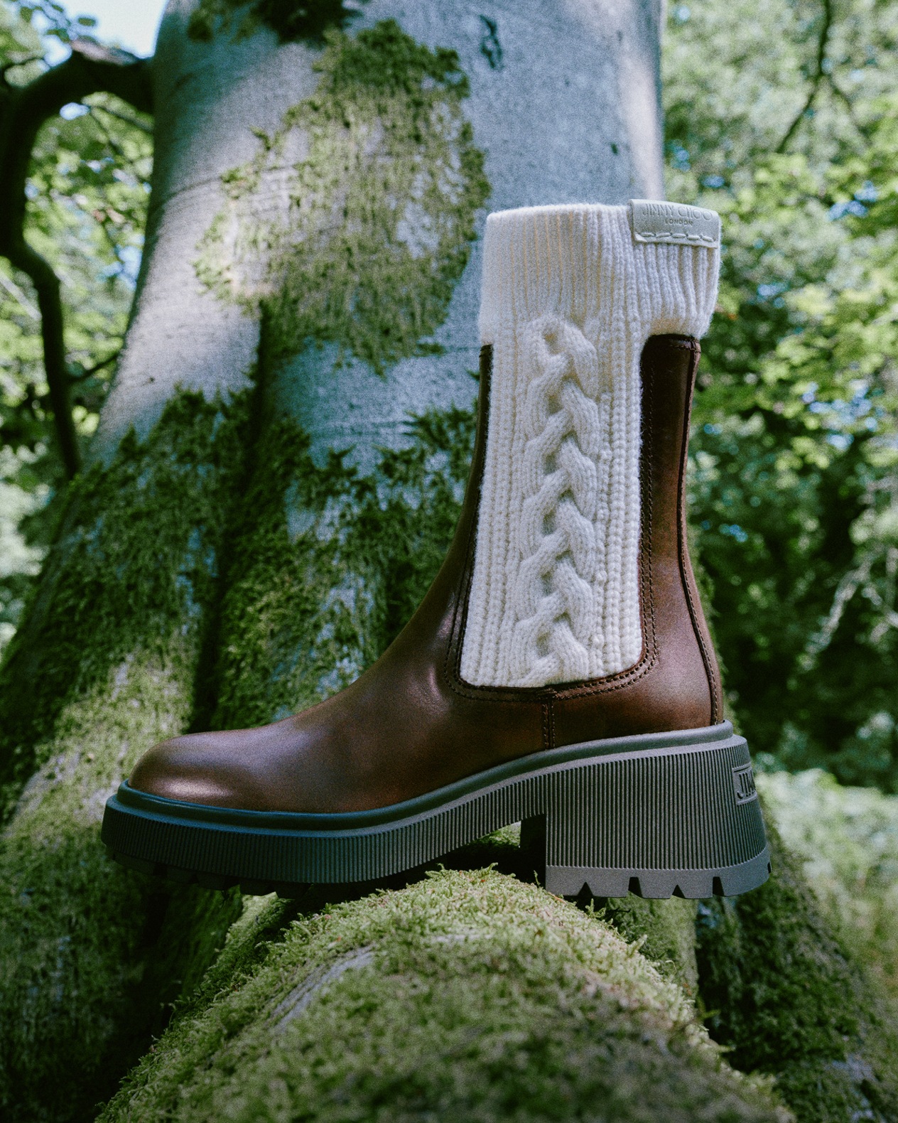 Cream knitted drawstring shoulder bag with leather strap, styled against textured tree bark in a natural forest setting. 