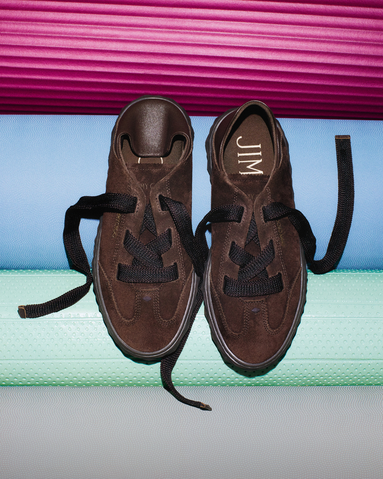 Brown leather pointed-toe pump with a sleek micro heel and silver buckle and pearl charm, displayed on stacked papers against a minimalist background.
