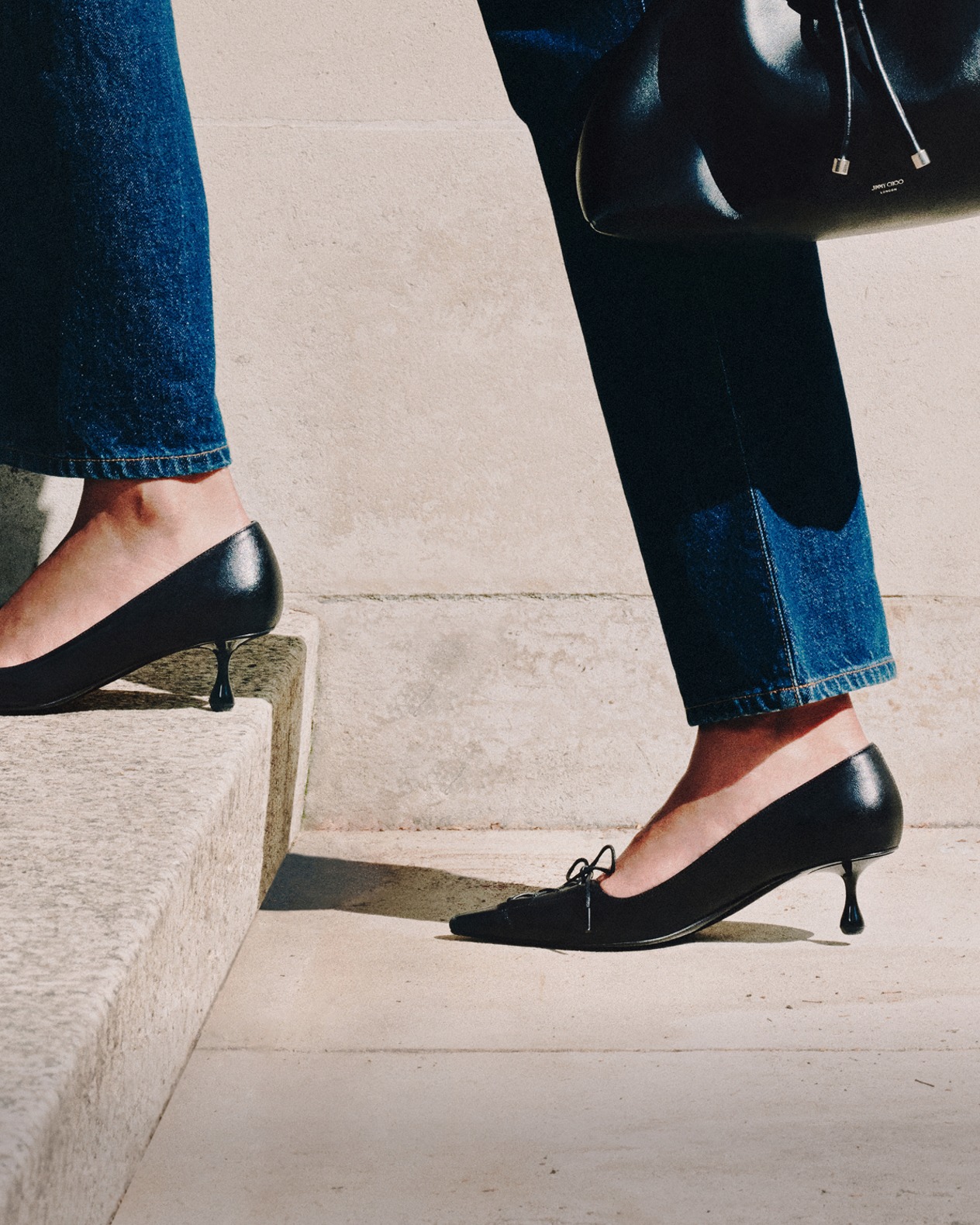 Brown leather pointed-toe pump with a sleek micro heel and silver buckle and pearl charm, displayed on stacked papers against a minimalist background.
