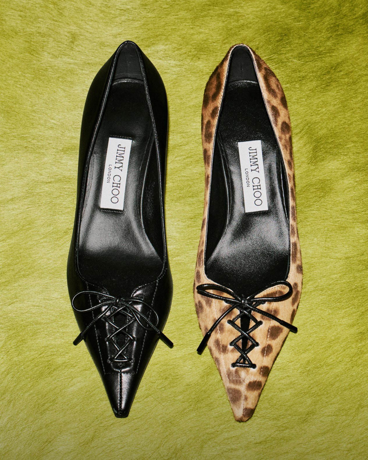 Pair of pointed-toe lace-up pumps, one in black leather and the other in leopard-print pony leather, displayed on a green textured surface.	