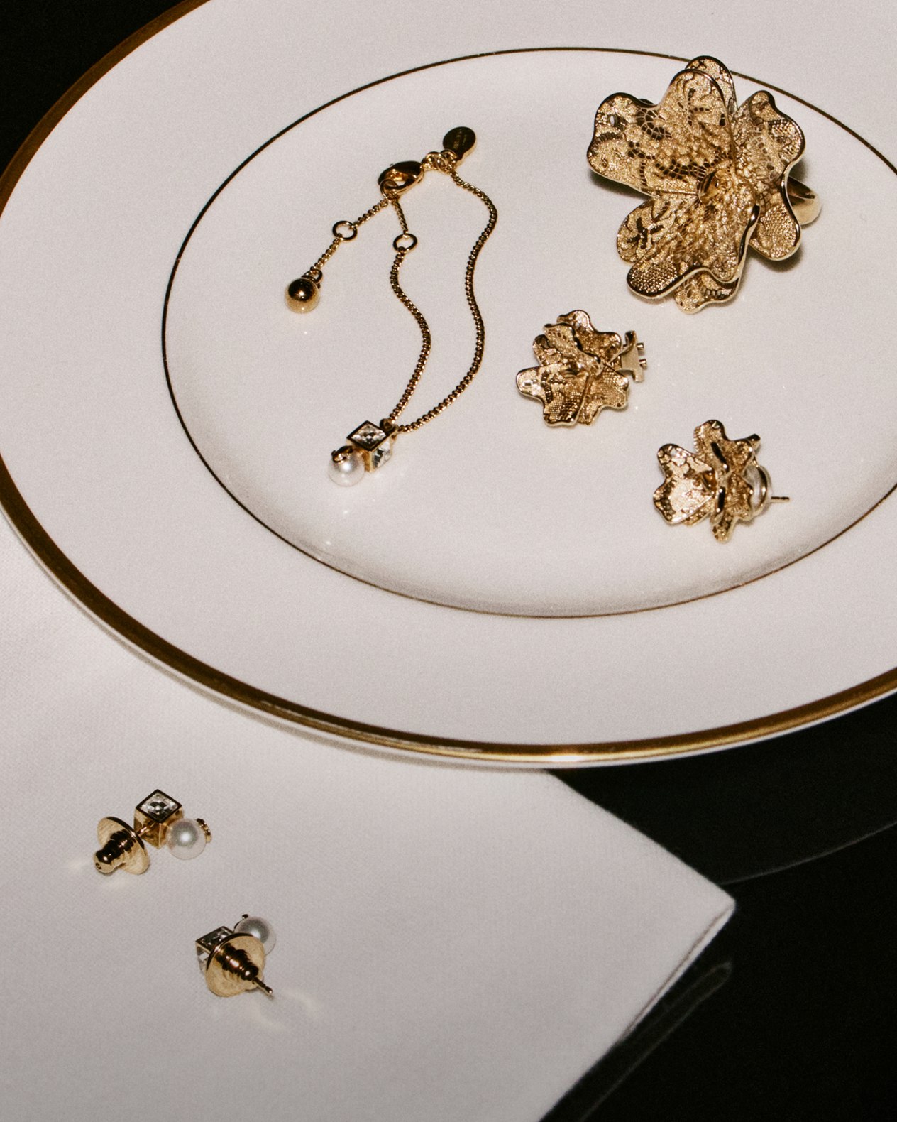 Gold floral jewellery pieces, including earrings and a bracelet with pearl accents, arranged on an elegant white and gold-rimmed plate.	