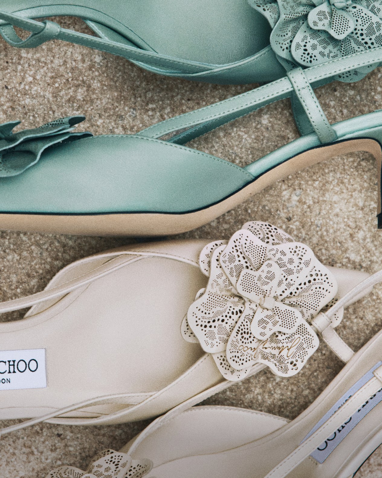 Two pairs of slingback pumps with floral appliqu&eacute; details, one in sage green and one in cream, displayed on a neutral textured surface.