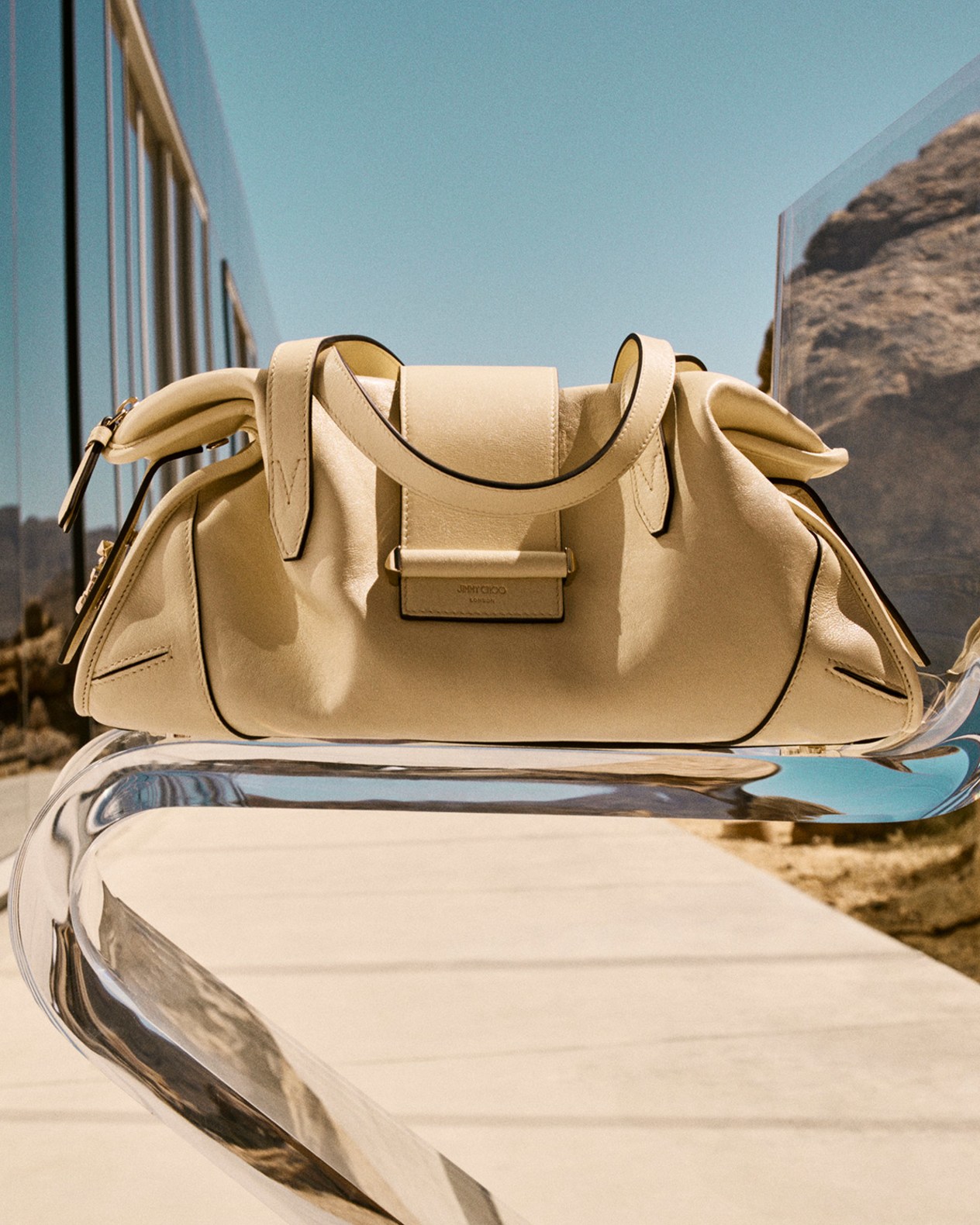 Mint green top-handle handbag with structured silhouette placed on a brick floor against a textured stone wall.	