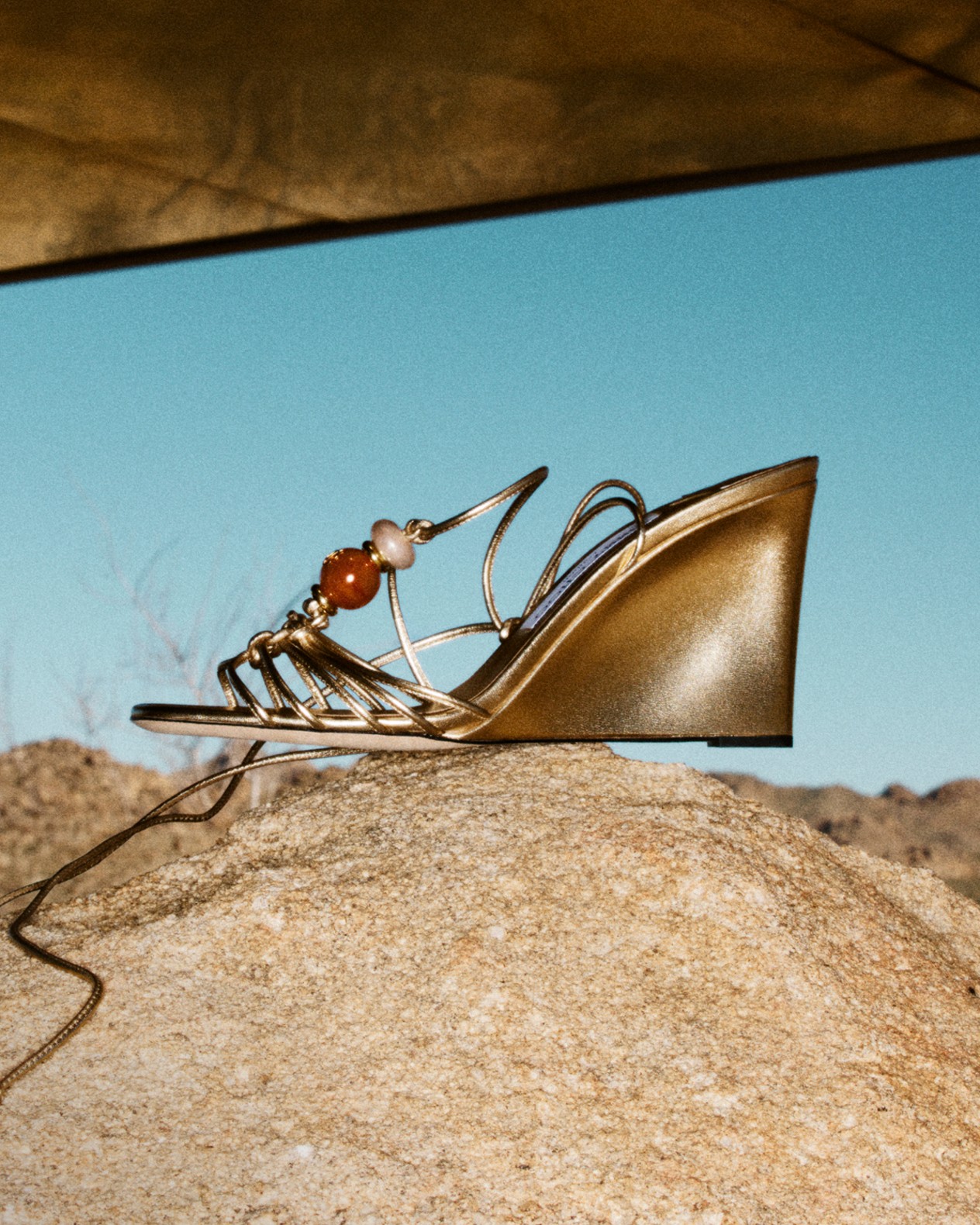 Beige flat sandals with textured fringe straps placed on rocky ground.