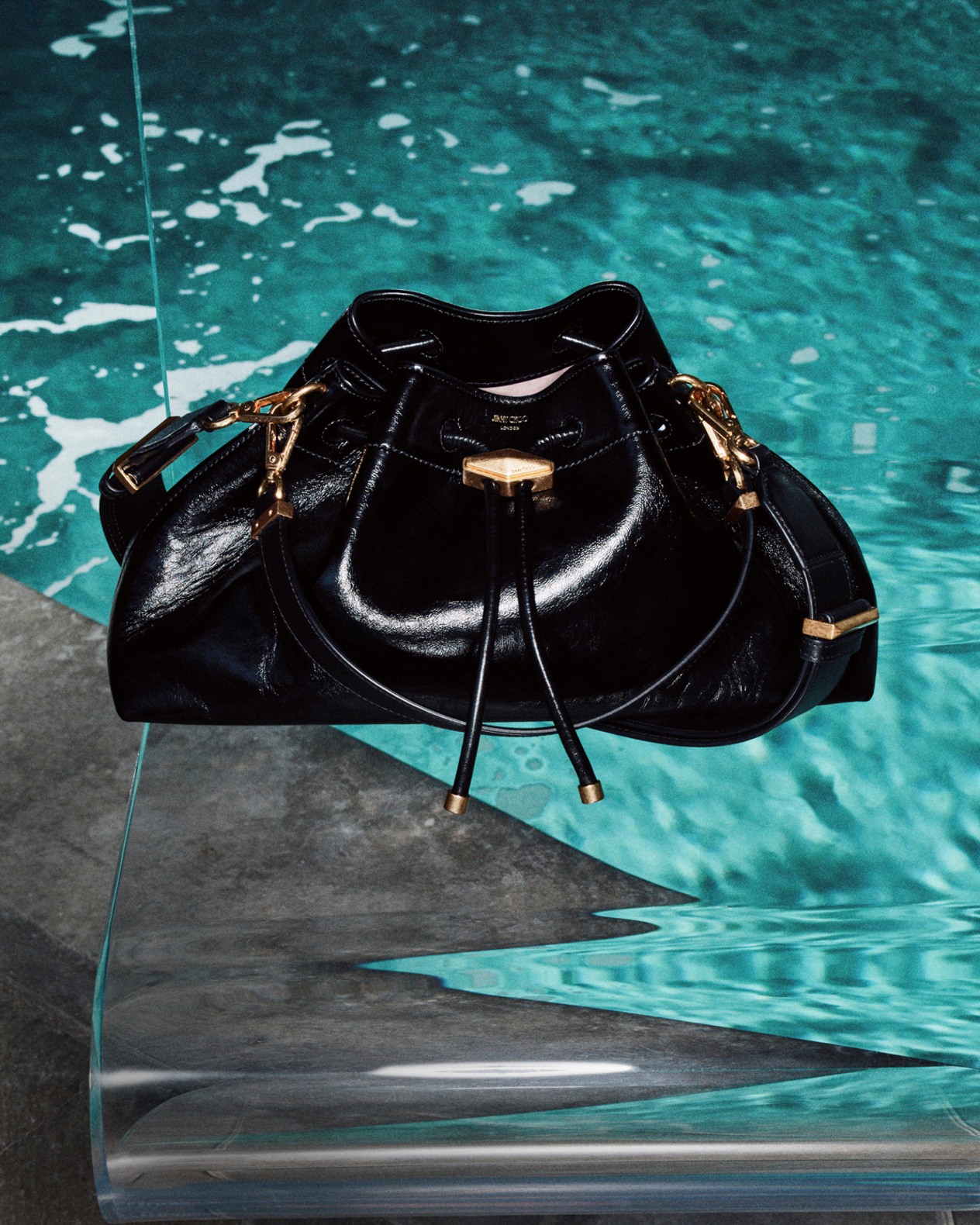 IMAGE ALT:Black leather drawstring bag with gold hardware placed beside a swimming pool.