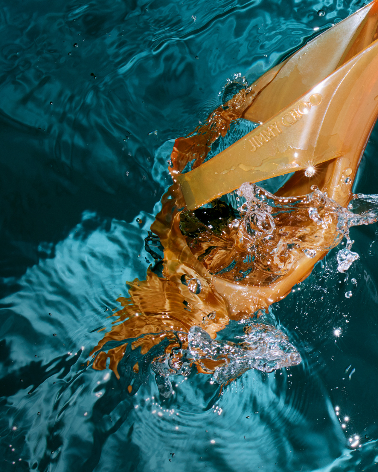 Orange jelly sandals splashing through turquoise water in a swimming pool.