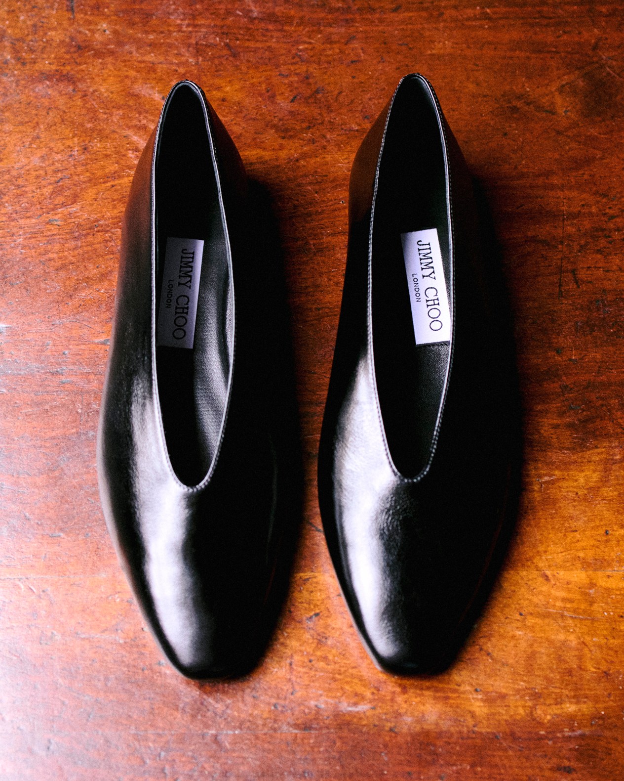 Pair of black leather ballet flats with square toes displayed on a wooden surface.