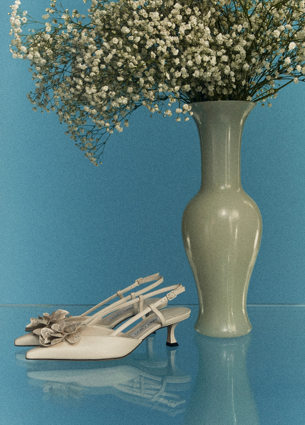 Ivory slingback heels with floral embellishment, styled beside a green vase with babys breath flowers.