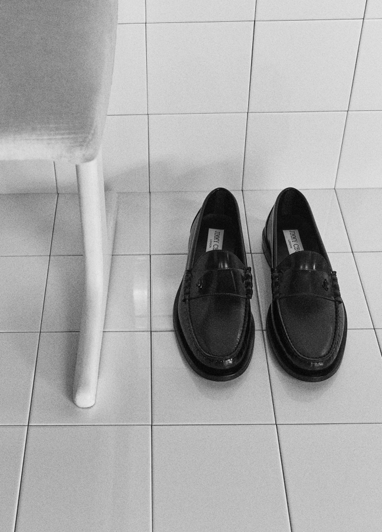 Black leather loafers placed on white tiled floor.