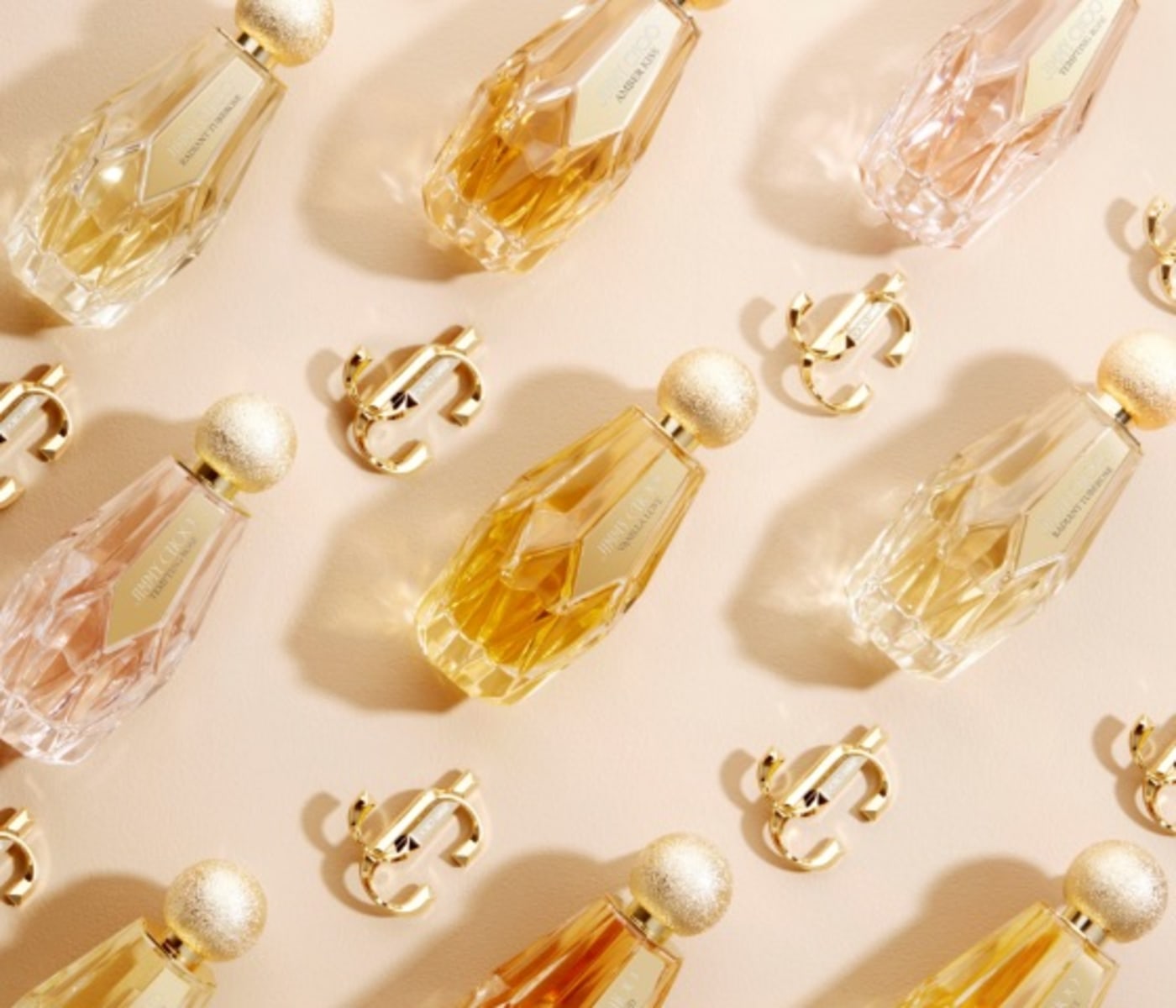 Three fragrances from the Jimmy Choo women&rsquo;s beauty collection lying next to gold JC emblems