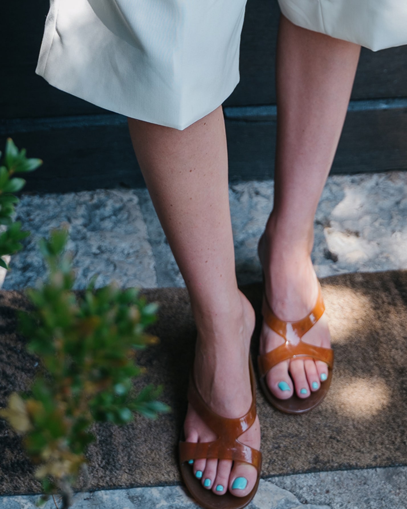 Close-up of amber sandals worn with a white shorts standing on a stone path.