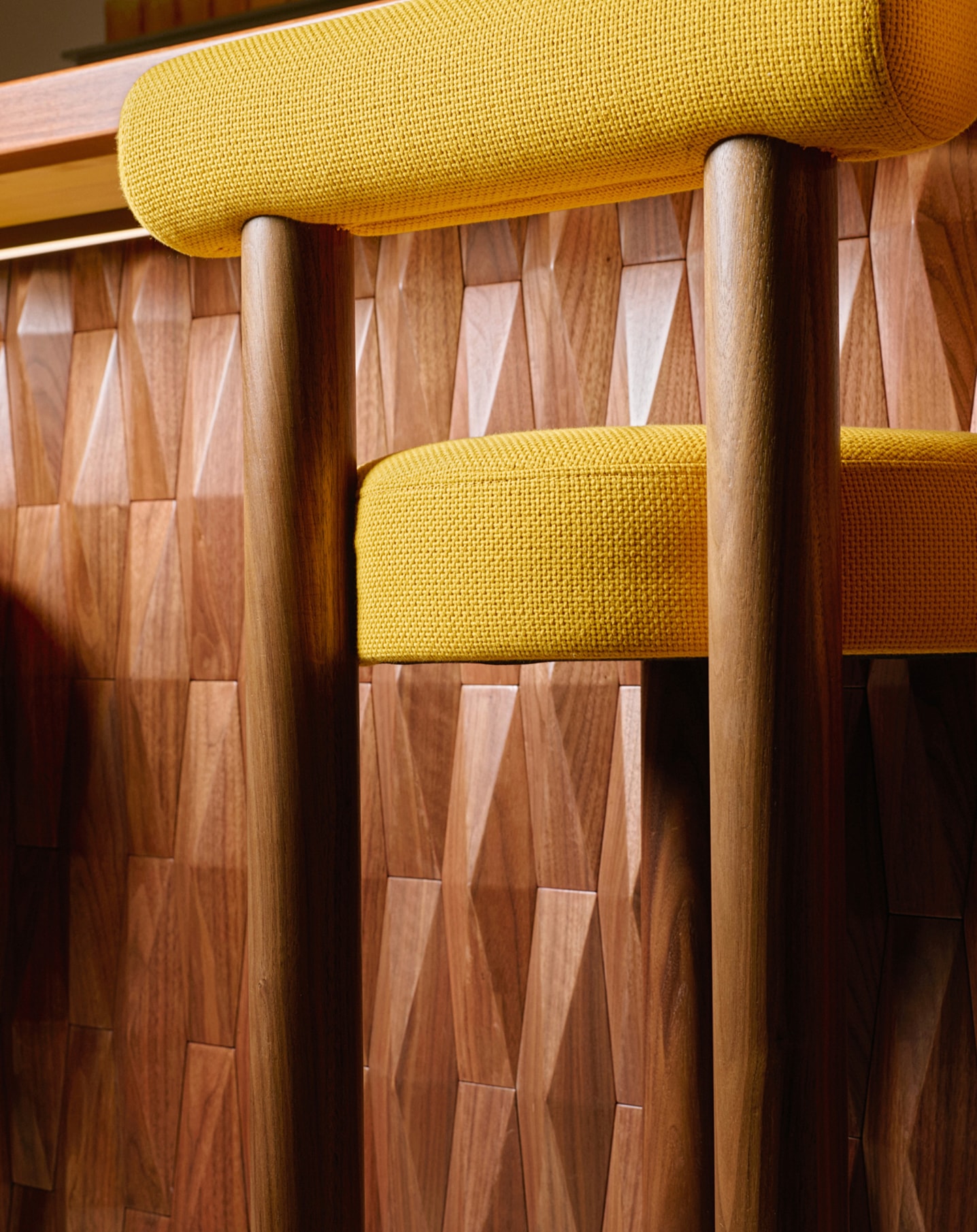 Close-up of a caf&eacute; table with yellow seating and a wooden tabletop holding a black menu and cutlery.