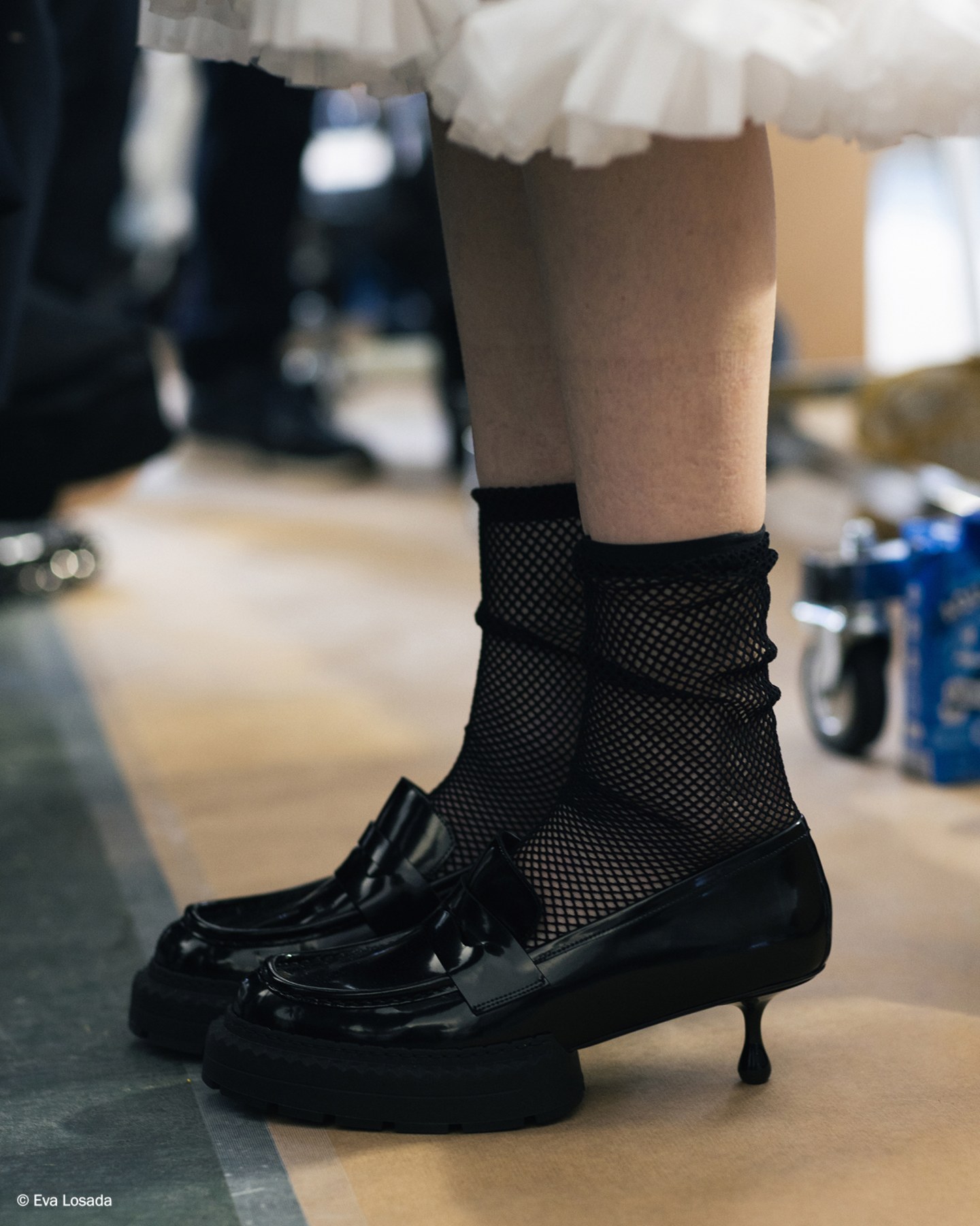 Black leather platform loafers worn with mesh socks and white ruffled skirt, photographed backstage.