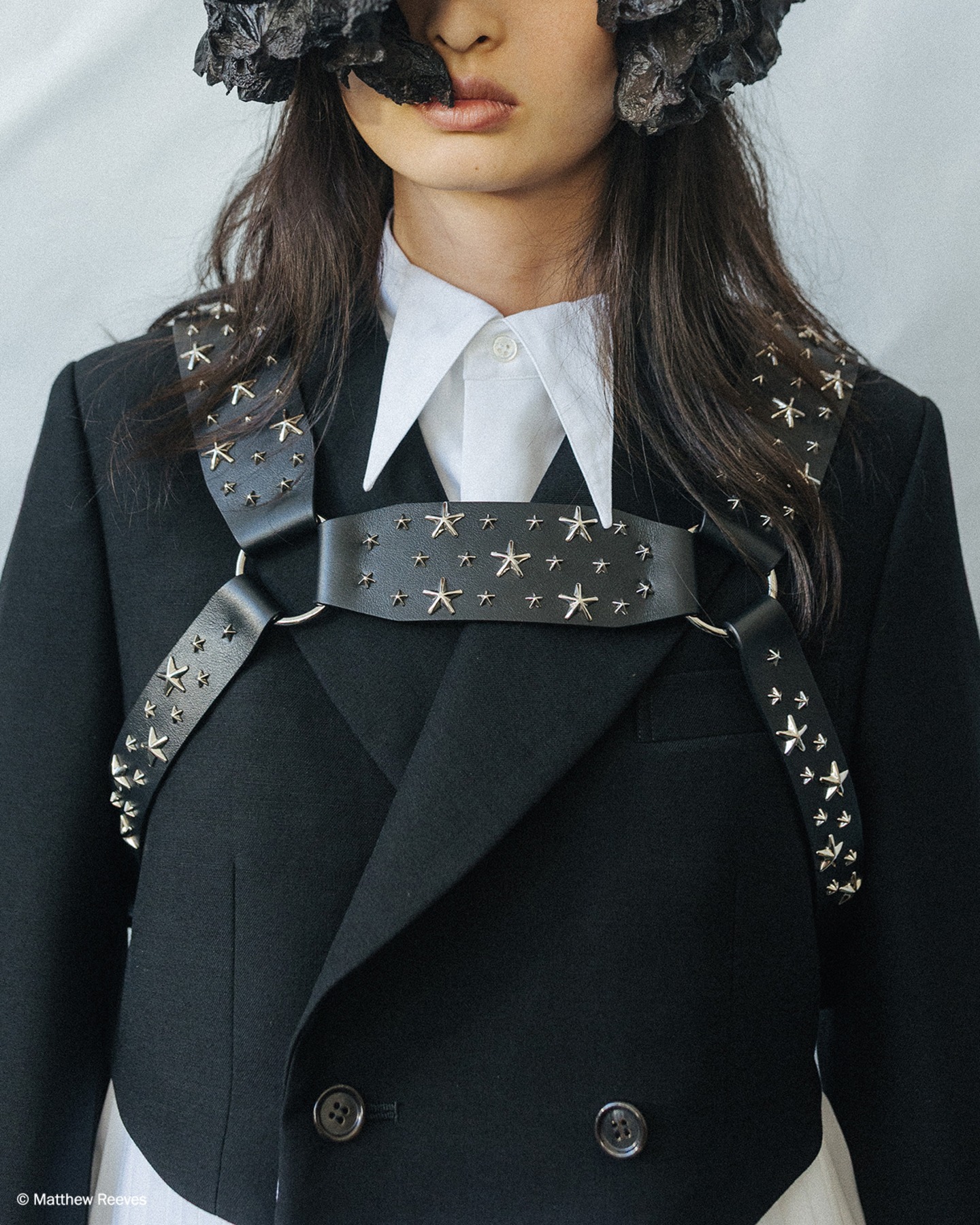 Close-up of a model wearing a black tailored jacket styled with a star-studded leather harness detail.