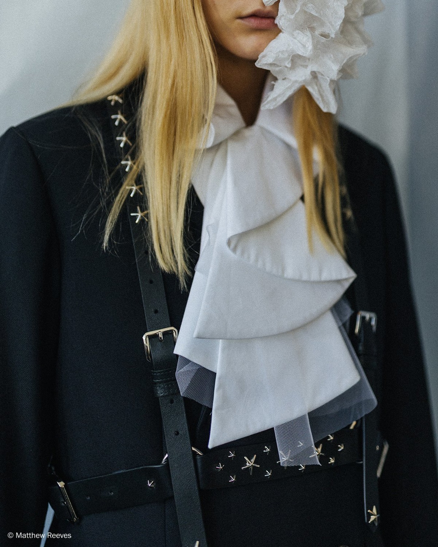 Close-up of black tailoring with ruffled white shirt and star-studded leather harness.
