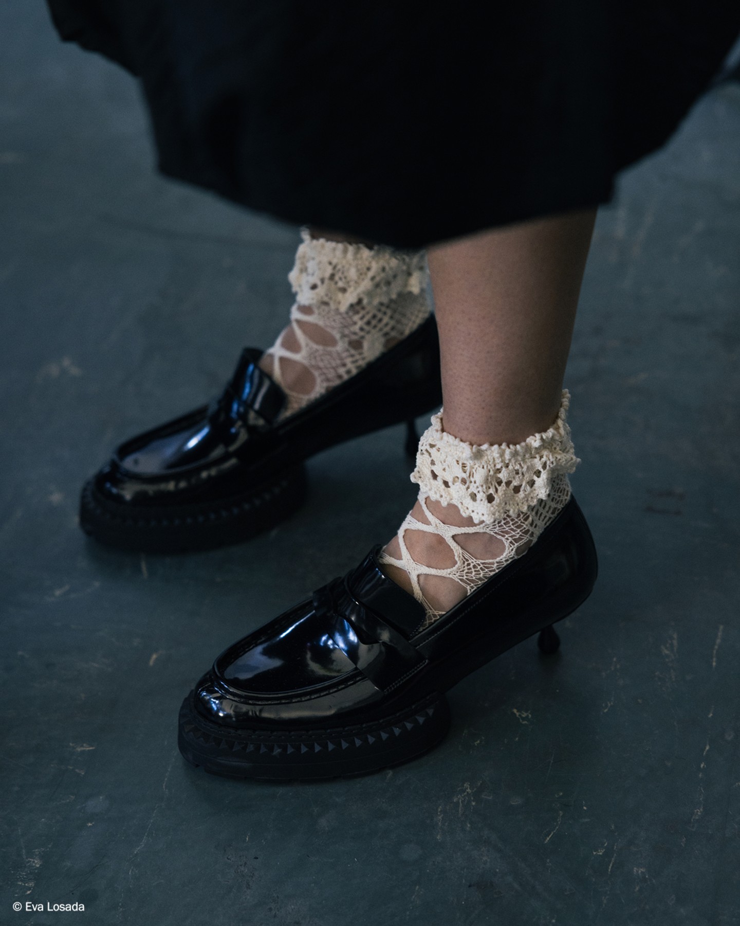 Black leather platform loafers worn with mesh socks and white ruffled skirt, photographed backstage.