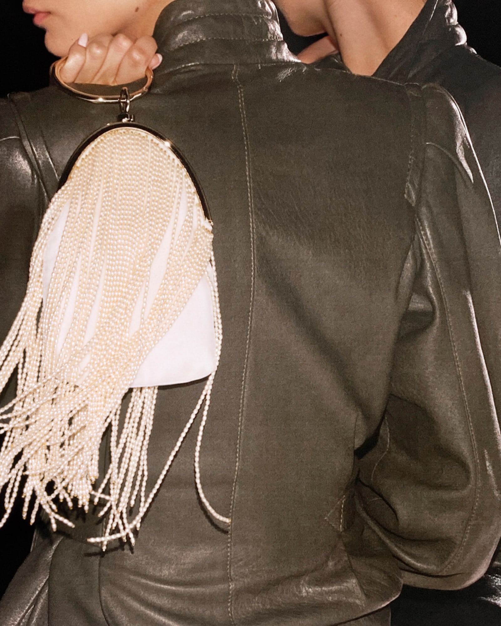 Close-up of a model in a black leather jacket carrying a white pearl-fringed bag with a gold-tone frame.