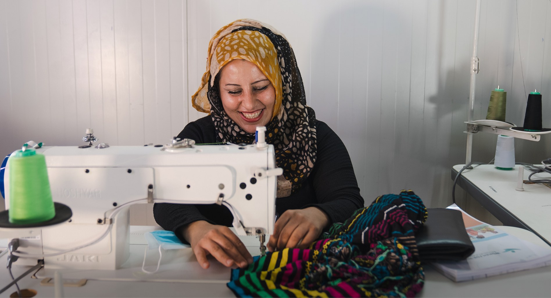Woman smiling while operating a sewing machine and working with colourful fabric.