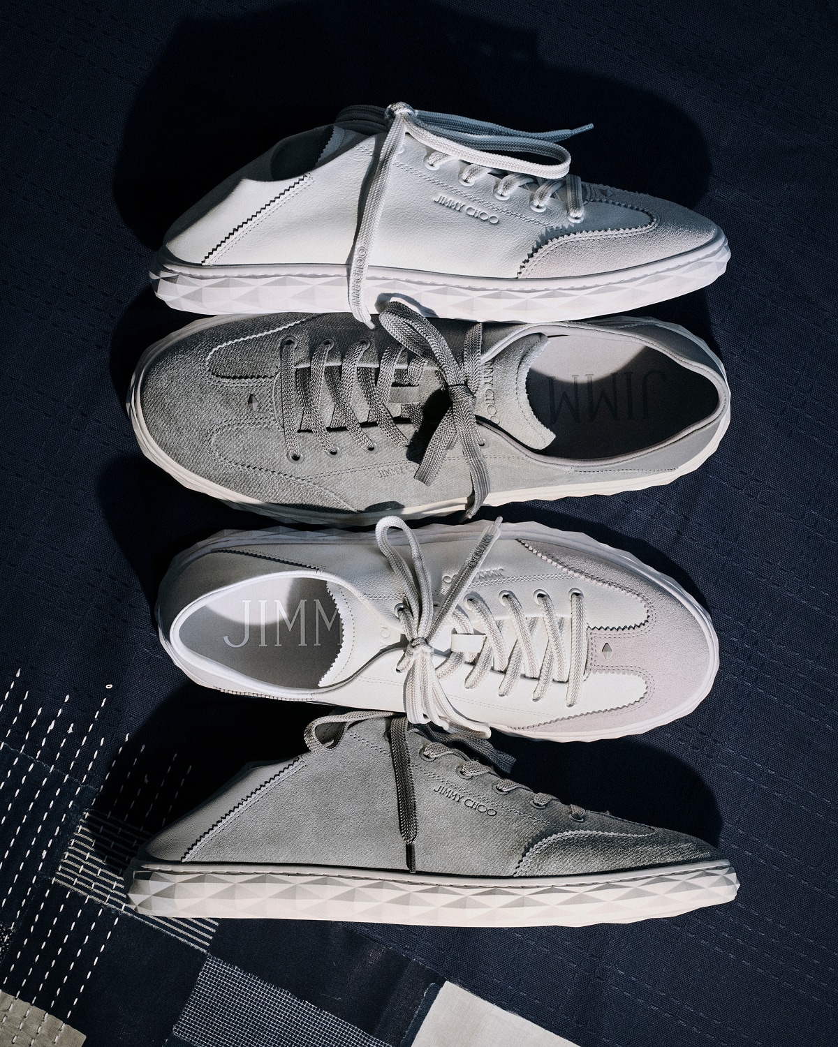 Stack of lace-up trainers in light and dark colourways arranged vertically against a dark background.